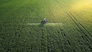 Areial shot of a farmer fertilizing a large green field of crops 