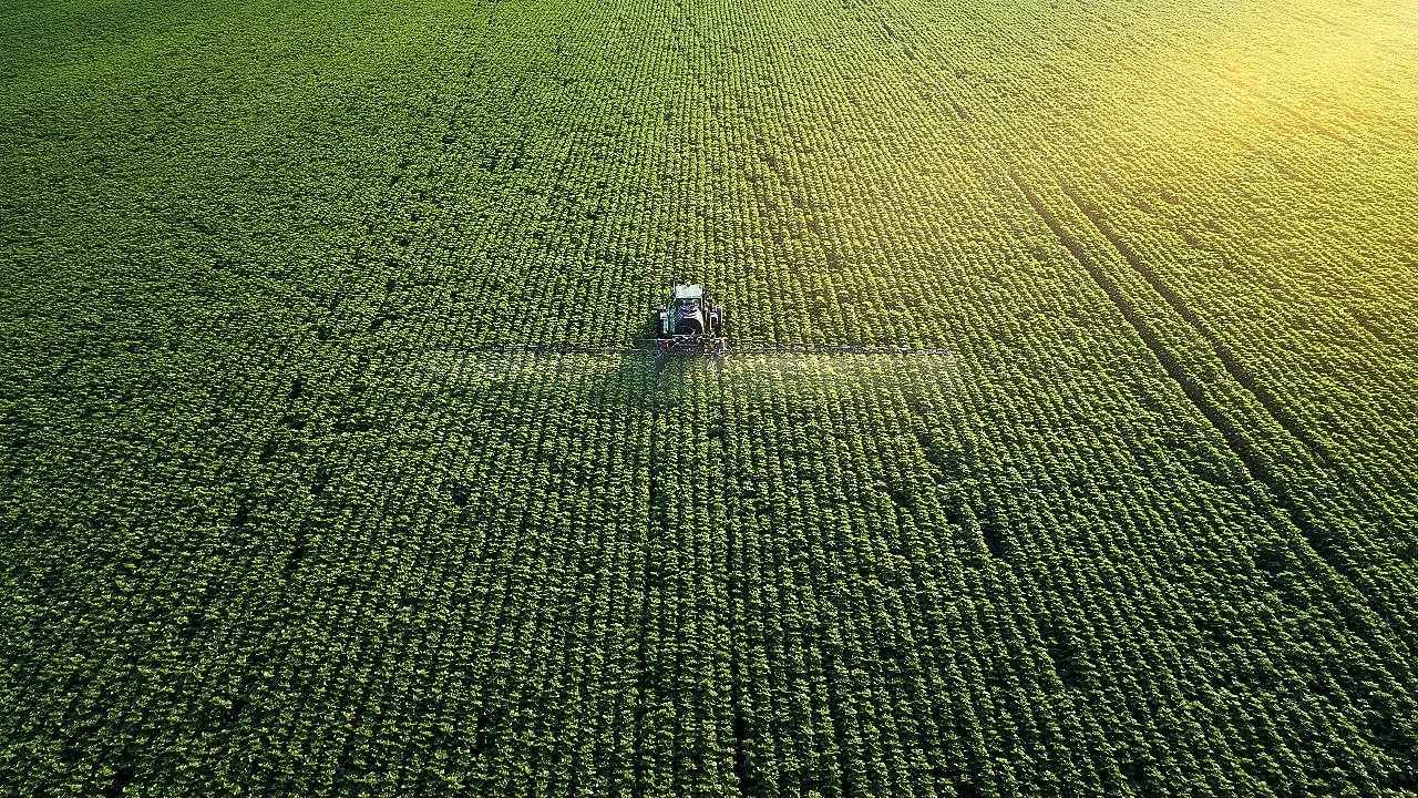 Areial shot of a farmer fertilizing a large green field of crops 
