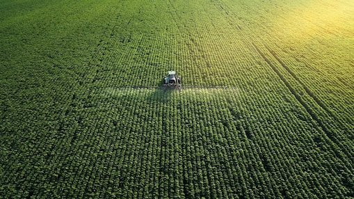 Areial shot of a farmer fertilizing a large green field of crops 