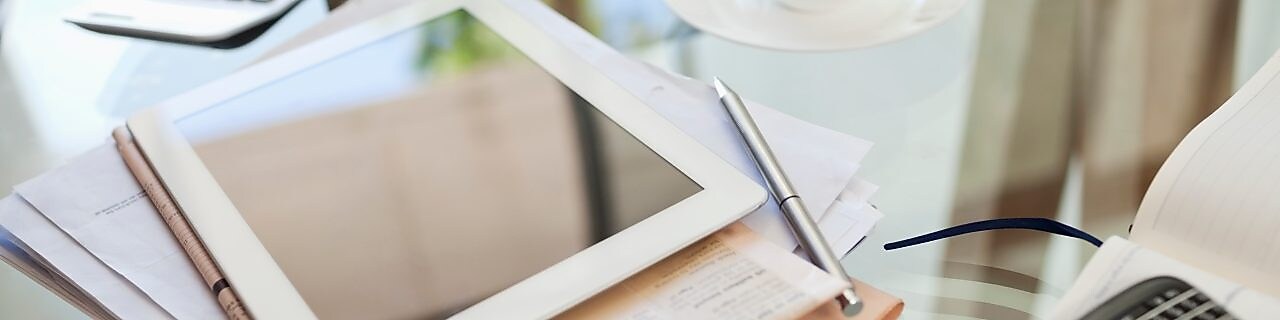 Tablet computer, newspaper, coffee cup and cell phone on desk