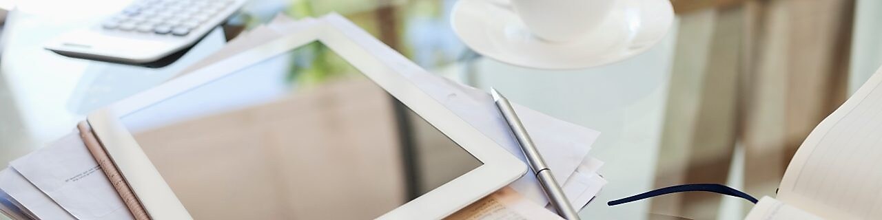 Tablet computer, newspaper, coffee cup and cell phone on desk