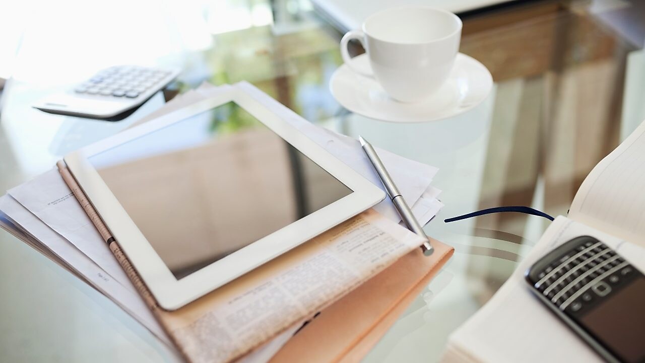 Tablet computer, newspaper, coffee cup and cell phone on desk
